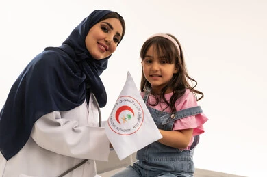 The relationships of affection and trust in the doctors of the Saudi Red Crescent Authority, an Arab Gulf Saudi female doctor in a hijab wearing a white medical coat stands next to a little girl, an Arab Gulf Saudi girl in casual attire holding the Saudi Red Crescent flag with pride and love, close-up portrait, white background, looking at the camera.