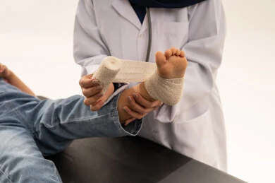 بورتريه مقرب لطبيبة عربية خليجية سعودية محجبة ترتدي المعطف الابيض الطبي تضع ضمادة طبية لتثبيت العظام , طفلة عربية خليجية سعودية ترتدي الزي الكاجوال ترفع قدمها لتلقي العلاج المناسب لها , خلفية بيضاء