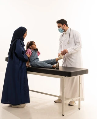 All specialties are available with high efficiency at the Saudi Red Crescent Authority. A Saudi Gulf Arab girl in casual attire is having her broken foot treated. A veiled Saudi Gulf Arab female doctor in a blue abaya is assisting the young girl. A competent Saudi Gulf Arab male doctor wearing a mask and a white medical coat is professionally performing his duties. Portrait with a white background, full-body.