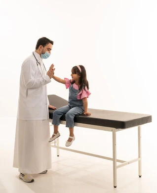 المصافحة بالكفين عالياً دليل على الفرحة لانتهاء الفحص الطبي و فترة العلاج , طبيب عربي خليجي سعودي يرتدي الكمامة للوقاية من الامراض و الزى الطبي الابيض , طفلة عربية خليجية سعودية ترتدي الزي الكاجوال تجلس على سرير الكشف في العيادة , بورتريه خلفية بيضاء , الجسم بالطول الكامل