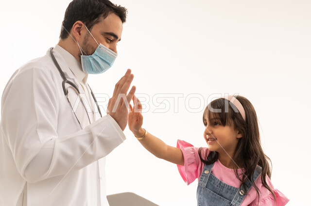 The concept of prevention is better than cure, an Arab Gulf Saudi doctor wearing a mask for protection against diseases, a small Arab Gulf Saudi girl wearing casual attire shaking hands with the doctor with her hands raised high as a sign of joy and happiness, close-up portrait, white background.