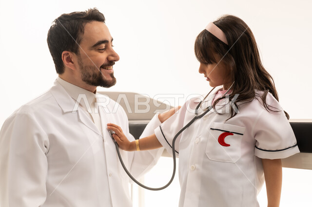 The concept of maintaining friendly relationships between patients and doctors while working seriously. An Arab Gulf Saudi doctor wearing a white medical coat plays the role of a patient and listens to the instructions of a little girl, an Arab Gulf Saudi child wearing a stethoscope and listening to the doctor's heartbeat in a playful manner, gestures of happiness and joy, close-up portrait, white background.