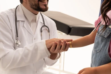 مصافحة ودية بين الطبيب و مريضته , طبيب عربي سعودي خليجي يرتدي امعطف الطبي الابيض يمسك بيد طفلة عربية خليجية سعودية ترتدي الزي الكاجوال , بورتريه مقرب , خلفية بيضاء