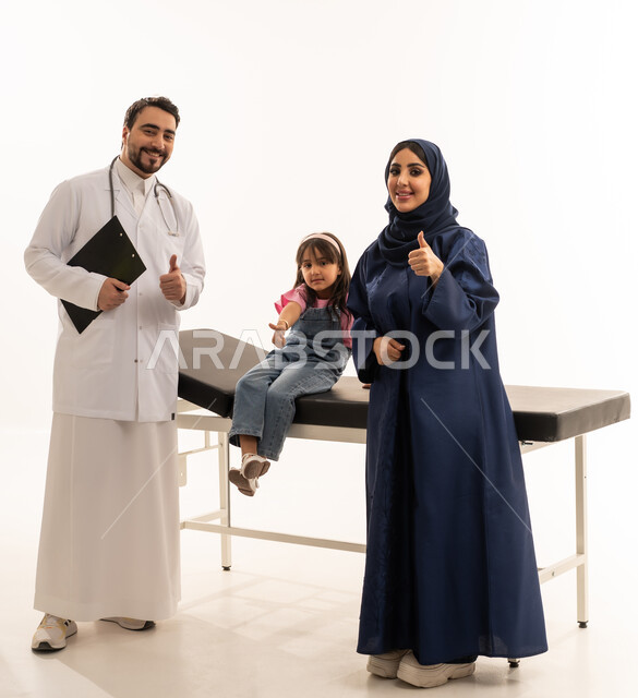 رفع اصبع الابهام لاعلى اشارة الى الجودة و الانتهاء من الفحص بنجاح , طفلة عربية خليجية سعودية ترتدي الزي الكاجوال تجلس على سرير الكشف الطبي بعد الاطمئنان على صحتها , طبيبة عربية خليجية سعودية محجبة ترتدي عباءة زرقاء تقف بسعادة مع الطبيب بعد الانتهاء من العمل , بورتريه خلفية بيضاء ,الجسم بالطول الكامل