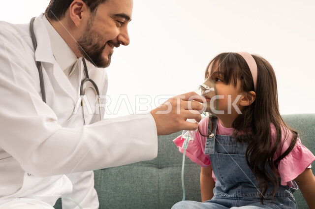 A Saudi Arabian Gulf Arab doctor wearing a white medical coat is helping the patient improve the inhalation process. A Saudi Arabian Gulf Arab girl dressed in casual attire is sitting on the clinic sofa wearing a breathing mask. White background, close-up portrait.
