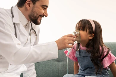 طبيب عربي خليجي سعودي يرتدي المعطف الطبي الابيض يقوم بمساعدة المريضة على تحسين عملية الاستنشاق , طفلة عربية خليجية سعودية ترتدي الزي الكاجوال جالسة على اريكة العيادة تضع القناع الخاص بالتنفس  ,خلفية بيضاء ,بورتريه مقرب