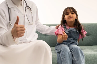 رفع اصبع الابهام للاعلى اشارة الى انجاز المهمة بجدارة ,طفلة عربية خليجية سعودية ترتدي الزي الكاجوال  تجلس مبتسمة على أريكة العيادة ,طبيب عربي خليجى سعودي يرتدي معطف طبي ابيض يرفع ابهامه علامة الجودة ,بورتريه مقرب, خلفية بيضاء