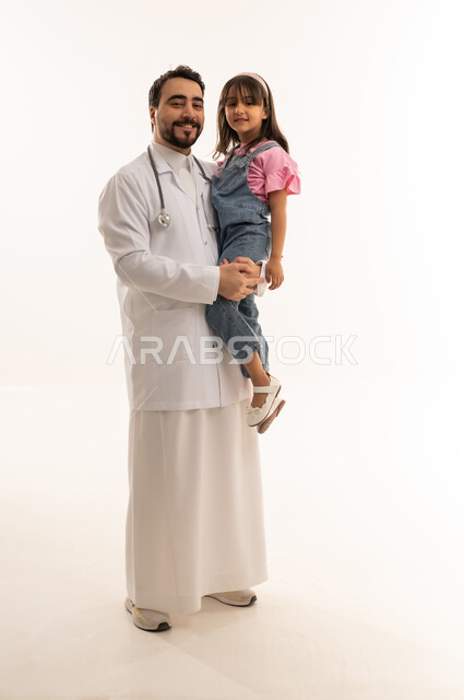أطباء هيئة الهلال الاحمر السعودي من الكفاءات المميزة ,طبيب عربي خليجي سعودي يرتدي المعطف الطبي الابيض يحمل طفلة صغيرة في سعادة ,طفلة عربية خليجية سعودية ترتدي الزي الكاجوال تبتسم للكاميرا ,بورتريه الجسم بالطول الكامل ,خلفية بيضاء
