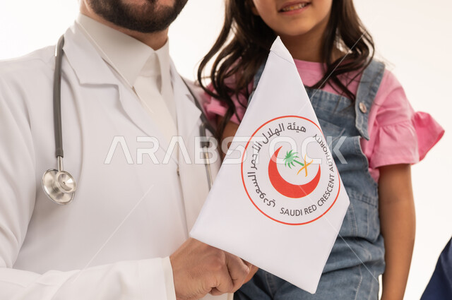A Saudi Arabian Gulf Arab doctor wearing a white medical coat holds the flag of the Saudi Red Crescent Authority, a symbol of trust and trained competencies. A Saudi Gulf Arab girl dressed in casual attire feels safe with her doctor. Close-up portrait, white background.