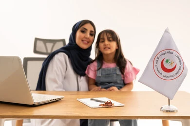 نظرة أمامية للكاميرا ,طبيبة عربية خليجية سعودية محجبة ترتدي المعطف الطبي الابيض تجلس بسعادة بعد الانتهاء من الفحص الطبي ,طفلة عربية سعودية خليجية صغيرة ترتدي الزي الكاجوال تجلس باطمئنان مع الطبيبة ,بورتريه مقرب , خلفية بيضاء