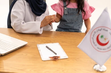 التأكد من سلامة صحة الاطفال الصغيرة ,طبيبة عربية خليجية سعودية محجبة تمسك يد الطفلة الصغيرة لطمأنتها ,بورتريه مقرب ليد طفلة صغيرة ترتدي الزي الكاجوال بعد الانتهاء من الفحص الطبي ,مفهوم الراحة و الأمان