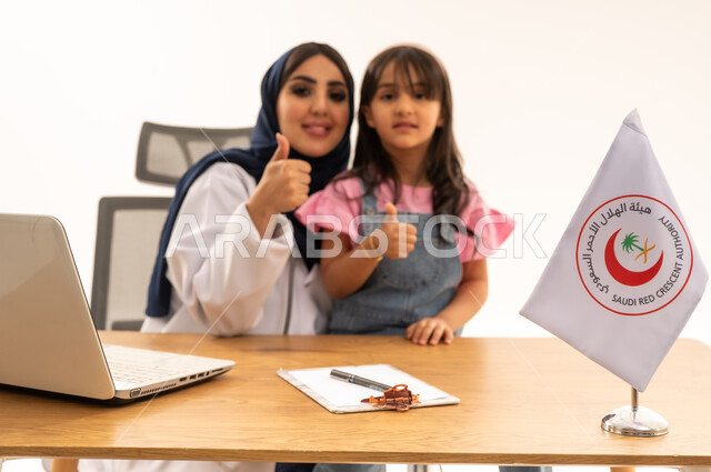طفلة عربية خليجية سعودية صغيرة ترتدي الزي الكاجوال تشعر بالطمأنينة مع الطبيبة المختصة ,طبيبة عربية خليجية سعودية محجبة ترتدي المعطف الطبي الابيض ,رفع اصبع الابهام علامة على الجودة واتمام العمل باحترافية
