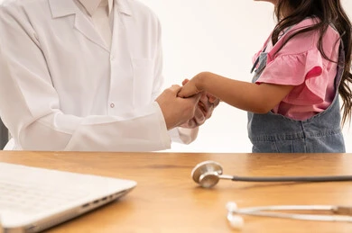 A Saudi Arabian Gulf Arab doctor wearing a white coat over a Saudi thobe is holding the hand of a Gulf Arab Saudi girl dressed in casual attire, finishing the examination and ensuring her health, close-up portrait, white background.