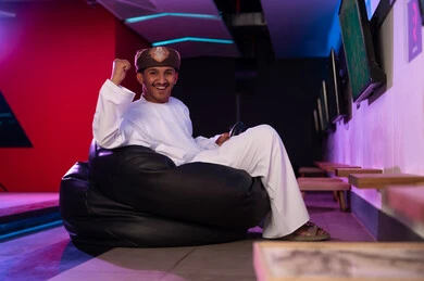 النظر للكاميرا بسعادة اثناء الاحتفال بالفوز , رجل عربي خليجي عماني يرتدي الدشداشة البيضاء و العمامة البنية يرفع قبضة يده للاعلى علامة على الفوز , ايماءات البهجة و السرور