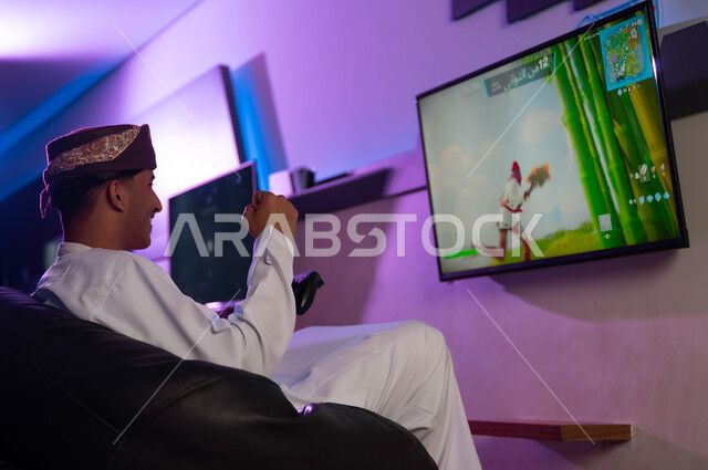 الاحتفال بالفوز فب اللعبة الالكترونية , رجل عربي خليجي عماني يرتدي الدشداشة البيضاء و العمامة يرفع قبضة اليد للاعلى علامة على الفرحة بالنصر , ايماءات السرور والبهجة