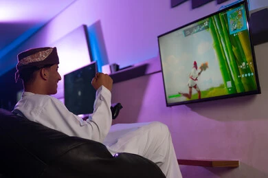 الاحتفال بالفوز فب اللعبة الالكترونية , رجل عربي خليجي عماني يرتدي الدشداشة البيضاء و العمامة يرفع قبضة اليد للاعلى علامة على الفرحة بالنصر , ايماءات السرور والبهجة