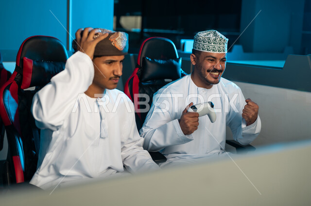 تعابير الفرحة و الاحتفال بالفوز في اللعبة الالكترونية , رجل عربي خليجي عماني يرتدي العمامة البنية و الدشداشة البيضاء يشعر بالحزن و الحسرة بعد الخسارة من الصديق , ايماءات سعادة و فرحة بالنصر, ايماءات حزينة