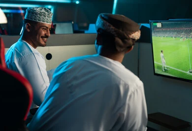 An enjoyable conversation among friends while playing inside the electronic games center, two Arab Gulf men from Oman wearing white dishdasha and turban, with embroidered cuffs, gestures of happiness and joy, entertaining youth activities. An enjoyable conversation among friends while playing inside the electronic games center, two Arab Gulf men from Oman wearing white dishdasha and turban, with embroidered cuffs, gestures of happiness and joy, entertaining youth activities.