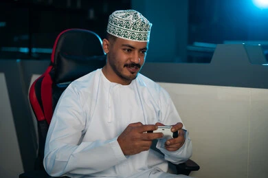 نشاط ترفيهي شبابي داخل مركز الالعاب الالكترونية , رجل عربي خليجي عماني يرتدي الدشداشة البيضاء و الكمة المطرزة يمسك جهاز التحكم عن بعد  , صورة مقربة