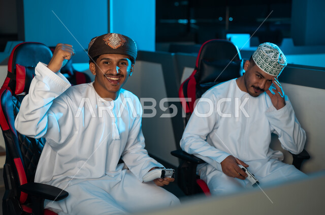 رجل عربي خليجي عماني يرتدي الدشداشة البيضاء و الكمة المطرزة يضع الكف على الوجه اشارة الي الحزن بعد الخسارة من صديقه , شاب عربي خليجي عماني يرتدي عمامة و دشداشة بيضاء يشعر بالسعادة بعد الفوز في اللعبة الالكترونية