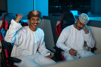 رجل عربي خليجي عماني يرتدي الدشداشة البيضاء و الكمة المطرزة يضع الكف على الوجه اشارة الي الحزن بعد الخسارة من صديقه , شاب عربي خليجي عماني يرتدي عمامة و دشداشة بيضاء يشعر بالسعادة بعد الفوز في اللعبة الالكترونية