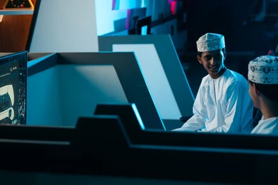 حديث ممتع بين الاصدقاء قبل بداية اللعبة الالكترونية , شابان عربيان خليجيان عمانيان يرتديان الدشداشة البيضاء و الكمة المطرزة يجلسان داخل الغرف الخاصة في مركز الالعاب الالكترونية , ايماءات السعادة و الابتسامة