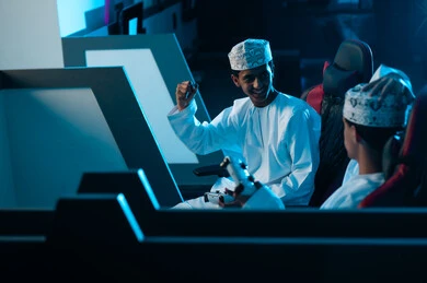 رفع قبضة اليد المقفولة لاعلى علامة على الفوز , شاب عربي خليجي عماني يرتدي الدشداشة البيضاء و الكمة المطرزة ينظر الى صديقه الخاسر , شاب عماني خليجي عربي ينظر الي صديقه الفائز بحزن شديد