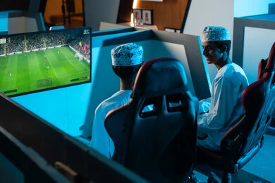 الاتفاق على اعضاء فريقين لعبة كرة القدم الشهيرة , شابان عربيان خليجيان عمانيان يرتديان الدشداشة البيضاء و الكمة المطرزة يتناقشان قبل بداية اللعبة الممتعة , الجلوس داخل غرفة خاصة بمركز الالعاب الالكترونية , انشطة شبابية ممتعة