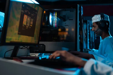 عرض اللعبة الالكترونية على شاشة الحاسب المكتبي , شاب عربي خليجي عماني يرتدي الدشداشة البيضاء و الكمة المطرزة يجلس بجانب صديقه , النقر على لوحة المفاتيح , ايماءات سعادة , صورة مقربة ,