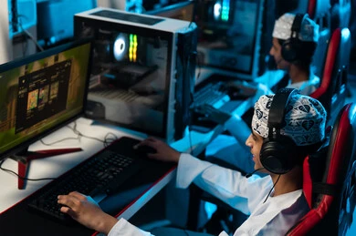 صديقان عربيان خليجيان عمانيان يرتديان الدشداشة البيضاء و الكمة المطرزة يلعبان الالعاب الالكترونية على جهاز الحاسب المكتبي , ايماءات السعادة و الفرحة بمشاركة الاصدقاء اوقات المرح ,