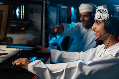 النظر الي شاشة الحاسب المكتبي بسعادة , شابان عربيان خليجيان عمانيان يرتديان الدشداشة البيضاء و الكمة المطرزة يجلسان على المقاعد الجلدية الحمراء , الاشارة باصبع السبابة الى الشاشة