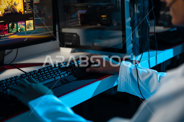 صورة مقربة لشاب عربي خليجي عماني يرتدي دشداشة بيضاء ينقرعلى لوحة مفاتيج الحاسب المكتبي , الالعاب الالكترونية المتعددة باستخدام الاجهزة التقنية الحديثة