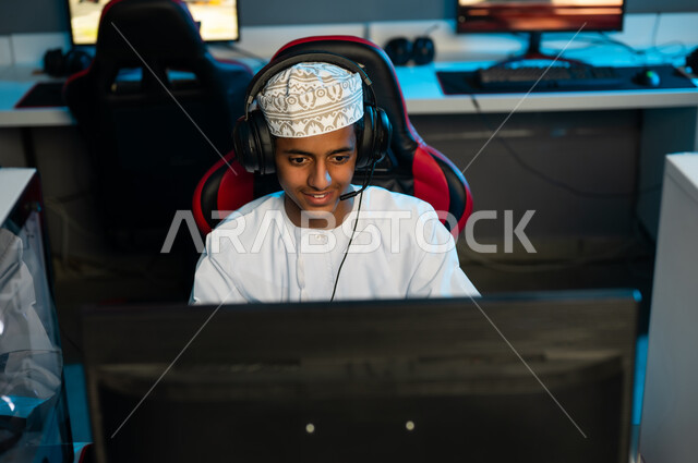 انشطة مختلفة مثيرة في مركز الالعاب الالكترونية , شاب عربي خليجي عماني يرتدي الدشداشة البيضاء و الكمة المطرزة يجلس على المقعد الجلدي الاحمر , قضاء اوقات ممتعة مع الاصدقاء