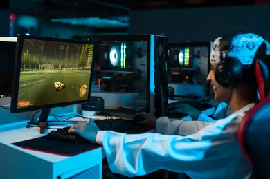 Gestures of happiness and a smile at the screen, a young Arab Gulf Omani man wearing a white dishdasha and a embroidered kumma, wearing headphones while playing, playing easily with friends from a distance.