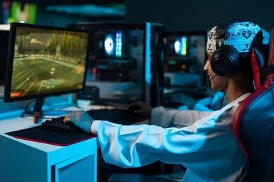 A young Arab Gulf Omani man wearing a white dishdasha and a embroidered kumma sits in front of a desktop computer, playing exciting electronic games, with a background image and headphones for easy communication with friends while playing.