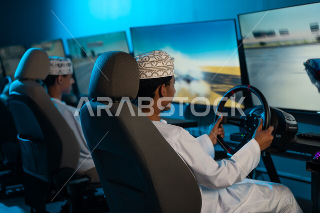The strong competition among friends, two young Arab Gulf Omanis wearing white dishdasha and embroidered kumma sitting behind the steering wheel, a collective youth activity, background image, looking at the screen.