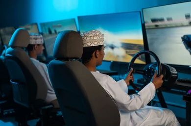 المنافسة القوية بين الاصدقاء , شابان خليجيان عربيان عمانيان يرتديان الدشداشة البيضاء و الكمة المطرزة يجلسان خلف عجلة القيادة , نشاط جماعي شبابي , صورة خلفية , النظر الي الشاشة