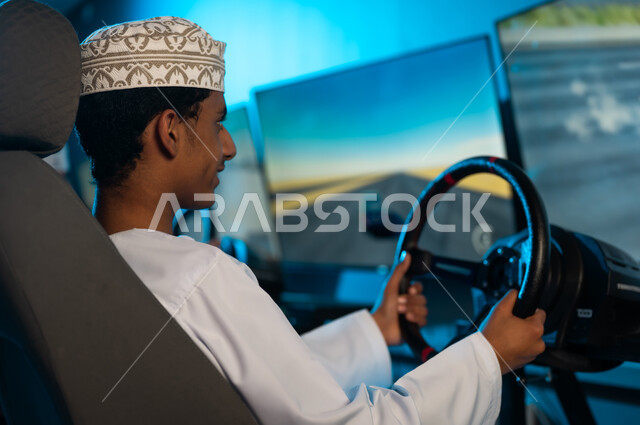 A young Arab Gulf Omani boy is looking at the racing screen with focus and enthusiasm, a background image of holding the steering wheel steadily, enjoyable youth activities, electronic games center.