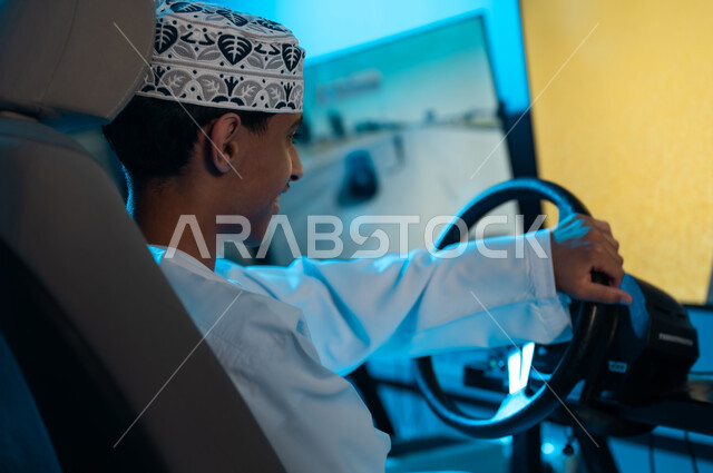 النظر الي الشاشة المعلقة بفرحة و ابتسامة , شاب عربي خليجي عماني يرتدي الدشداشة البيضاء و الكمة المطرزة يمسك مقود السيارة , التنافس و الحماس بين الاصدقاء , صورة خلفية