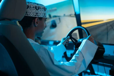 Spending enjoyable times at the electronic games center, a young Arab Gulf Omani man wearing a white dishdasha and a embroidered kumma sits in the driver's seat, gestures of happiness and joy.