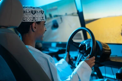 ايماءات الفرحة و الابتسامة اثناء النظر الي الشاشة , شاب عربي خليجي عماني يمسك عجلة القيادة بثبات , التركيز للفوز بالمركز الاول , صورة مقربة