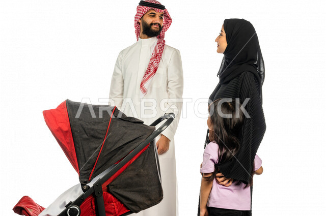 Portrait of a Saudi Arabian Gulf man pulling a stroller with his wife and young daughter with gestures indicating happiness and love, emotional bonding, the concept of a happy family, a family picnic and a tour, spending fun family times