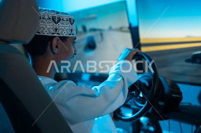 تعابير الحماس و الاثارة اثناء لعب سباق السيارات , شاب عربي خليجي عماني يرتدي دشداشة بيضاء و كمة مطرزة يجلس خلف عجلة القيادة , انشطة شبابية مثيرة , صورة مقربة