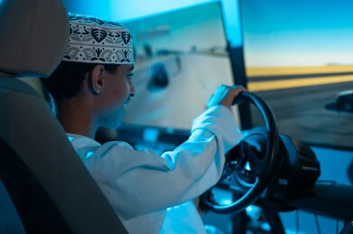 تعابير الحماس و الاثارة اثناء لعب سباق السيارات , شاب عربي خليجي عماني يرتدي دشداشة بيضاء و كمة مطرزة يجلس خلف عجلة القيادة , انشطة شبابية مثيرة , صورة مقربة