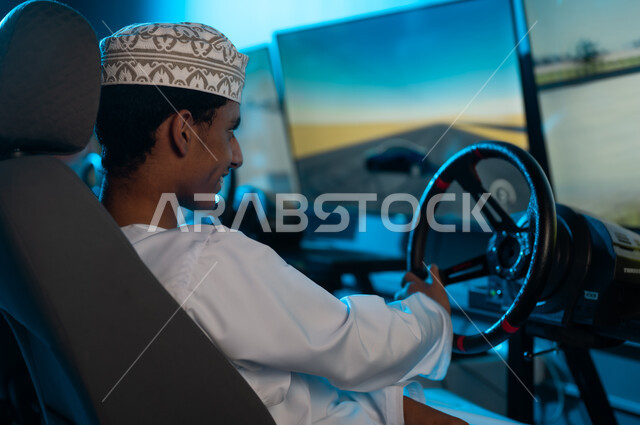 Holding the steering wheel, a young Arab Gulf Omani man wearing a white dishdasha and a embroidered kumma looks intently at the screen, gestures of smiles and happiness, close-up shot, fun games in the electronic games center.
