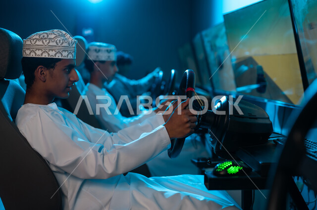 لعبة محاكاة سباق السيارات داخل مراكز الالعاب الالكترونية , شباب عربي خليجي عماني يرتدي دشداشة بيضاء و كمة مطرزة ينظرون الى شاشات عرض اللعبة , المنافسة بين الاصدقاء و قضاء الاوقات المسلية