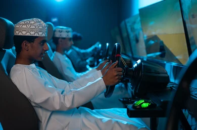 لعبة محاكاة سباق السيارات داخل مراكز الالعاب الالكترونية , شباب عربي خليجي عماني يرتدي دشداشة بيضاء و كمة مطرزة ينظرون الى شاشات عرض اللعبة , المنافسة بين الاصدقاء و قضاء الاوقات المسلية