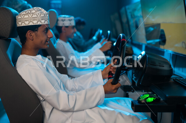 A group of young Arab Gulf Omanis wearing white dishdashas and embroidered kumas, sitting in front of screens playing car racing games, engaging in collective youth activities, looking with focus and professionalism to achieve victory.