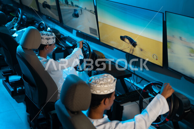 النظرالي الشاشات بتركيز للفوز في سباق السيارات , مجموعة من الشباب العربي الخليجي العماني يرتدي الدشداشة البيضاء و الكمة المطرزة يجلسون على مقعد السائق , العاب ممتعة واجواء شبابية