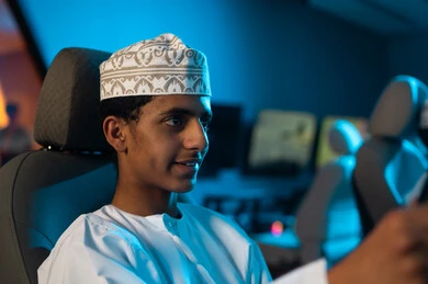 النظر للشاشة بتركيز و ثبات لتحقيق العامة الكاملة , رجل عربي خليجي عماني يرتدي دشداشة بيضاء و كمة مطرزة يجلس على مقعد ساثق سباق السيارات , ألعاب محاكاة الواقع الحقيقي , صورة مقربة